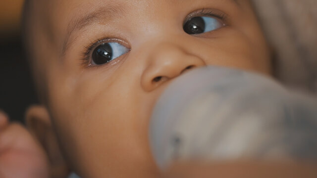 Close up, dark skin baby drinking milk from the bottle in mothers hands. High quality photo