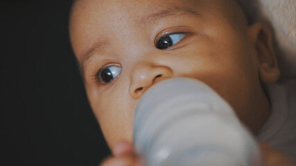 Portrait of multiracial baby drinking his formula from plastic bootle. Close up. High quality photo