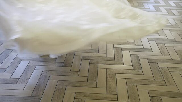 The groom in a gray suit and black patent leather shoes picks up the bride in a lush wedding dress with lace and twists her around him in a bright large expensive restaurant on the parquet