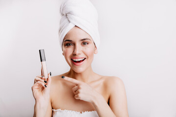 Green-eyed young girl in white towel with smile points to concealer hiding all imperfections of skin