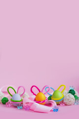 Fototapeta na wymiar Set of colorful eggs with Easter bunny ears lie near the ribbon and ornaments on a pink background. Vertical banner. Postcard for the Easter holiday. Copyspace