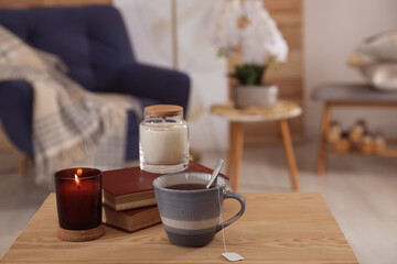 Cup of tea, books and candles on wooden table in living room. Interior design
