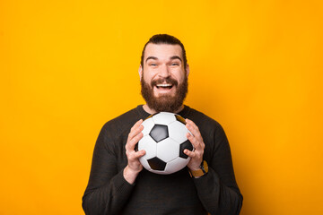 Portrait of happy bearded man holding soccer ball over yellow background.