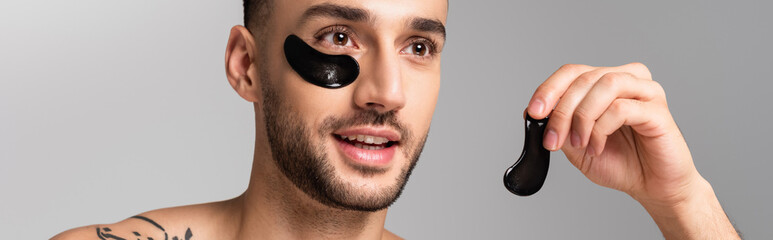 Obraz premium young smiling hispanic man holding eye patch isolated on grey, banner