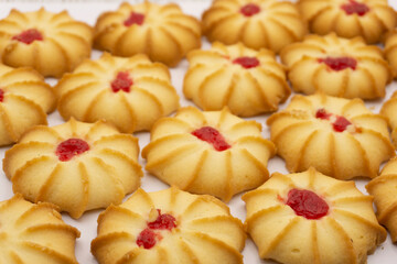 Shortbread cookies with jam in the middle on white plate against brown background .