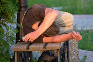 Homeless man fallen down on the ground next to a bench in the park, experiencing lethargy after excessive drinking .