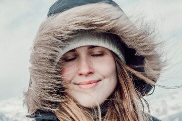 woman in a hood, wind in her hair, closed eyes, smile, winter