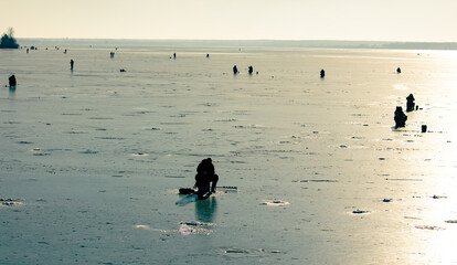 Silhouettes of fishermen on the ice of the lake