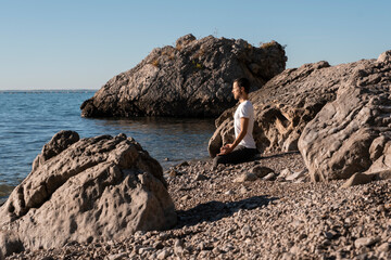 Attractive young man practicing yoga meditation and breathwork outdoors by the sea