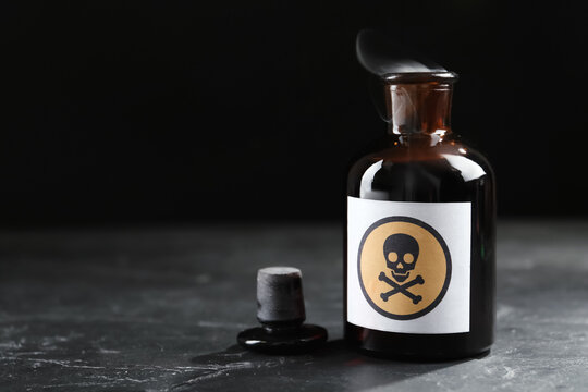 Open glass bottle of smoking poison with warning sign on black table. Space for text