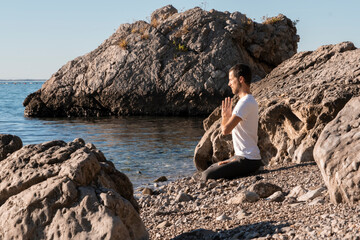 Attractive young man practicing yoga meditation and breathwork outdoors by the sea