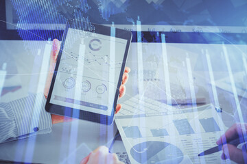 Double exposure of man's hands holding and using a digital device and forex graph drawing. Financial market concept.