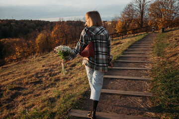 Young cheerful woman with bouquet of camomiles flowers on golden our. Millennials, Gen z, young and beautiful