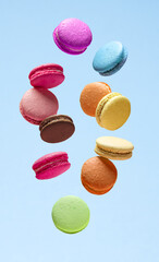 Colorful sweet macarons or macaroons, flavored cookies floating in the air on blue background.