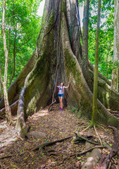 Young woman standing near old Kapok tree, with big roots in the jungle. Arenal Volcano National Park. Costa Rica, Central America.