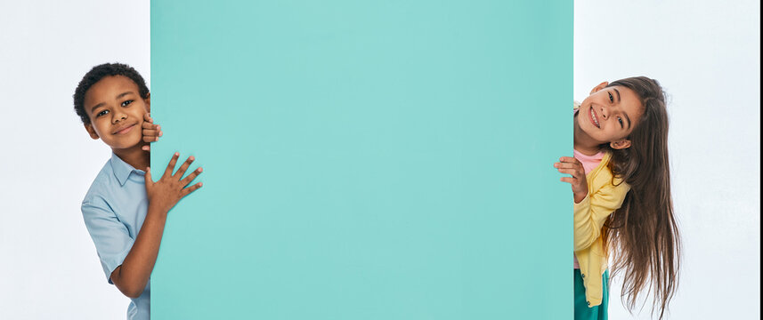 Multi-ethnic children peeking from behind an empty turquoise wall. Empty space for text with kids