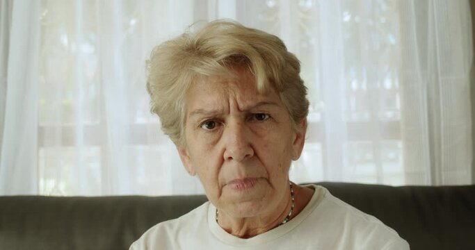 A medium close-up shot of an elderly woman after retirement cut short hair with light brown hair is showing a displeasure expression.