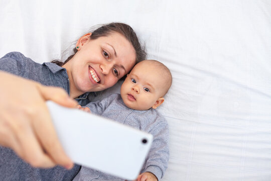 Mom with newborn baby take selfie while lying on the bed
