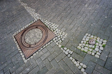 Old pavement in the city. A sewer manhole and a small cobblestone. A combination of a square ..and a circle.