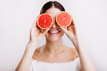 Cute attractive dark-haired girl with charming smile poses, covering her eyes with grapefruits