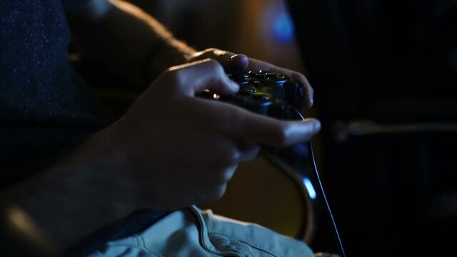 Close view of a gamer's hands playing soccer (football) simulator video game on console using joystick.