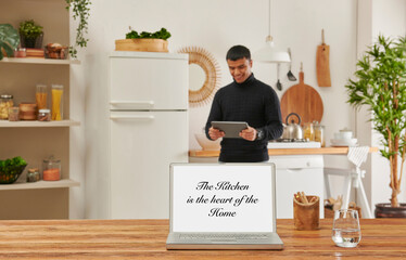 Close up laptop screen on the wooden table, kitchen background with man using tablet and drink coffee.