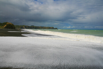 Black volcanic sand and stones Beach with ocean water foam and waves, Whirinaki Beach, Hawke's Bay, Napier, North Island of New Zealand