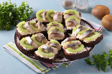 Homemade sandwiches with kiwi, herring, cream cheese and garlic on a light blue background. Horizontal format
