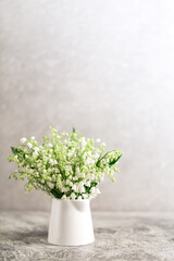 bouquet of lilies of the valley in a white glass on a gray concrete background