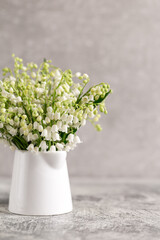 bouquet of lilies of the valley in a white glass on a gray concrete background
