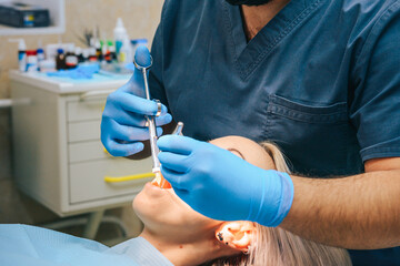 A girl at the reception of a male dentist in a dental chair, with her mouth open during an injection of painkillers.