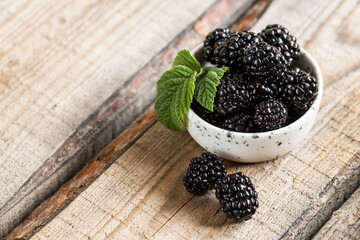 fresh juicy blackberries with green leaves in a plate on a wooden table. healthy berry, antioxidants, antiage foods