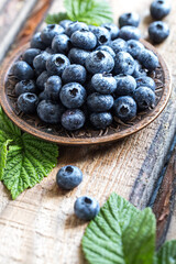 fresh juicy blueberries with green leaves in a plate on a wooden table. healthy berry, antioxidants, antiage foods
