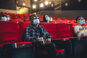 People sit in the cinema hall and watch a movie wearing medical masks and keep their distance....