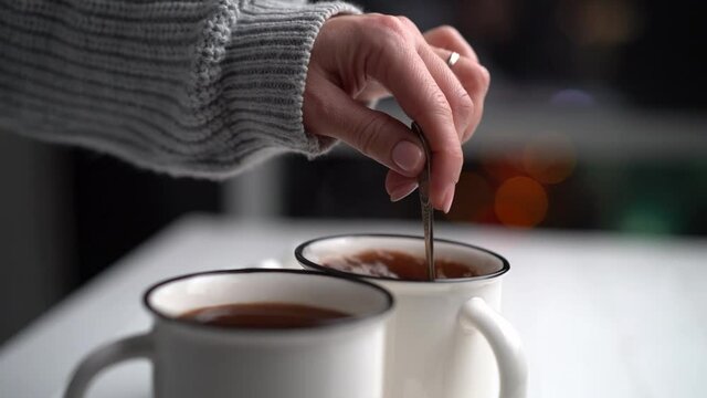 Woman stirring cacao in white mug using teaspoon