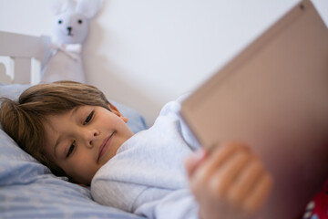 Boy Playing Video Games. A Boy Lying On His Bed Playing With His Tablet.Technology
