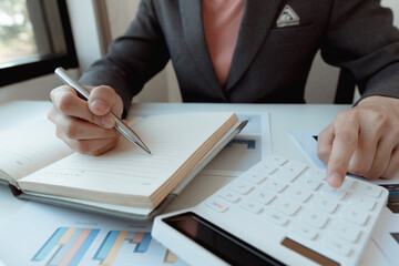 Business accountants are taking notes in notebooks and using a calculator to calculate financial costs.