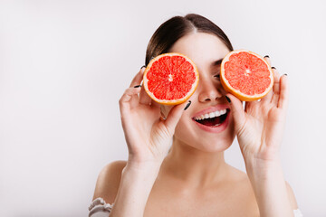 Closeup portrait of dark-haired woman smiling and holding grapefruits in front of eyes on isolated background