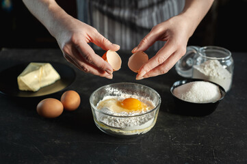 The process of preparing the dough. The woman breaks the egg and adds it to a bowl of flour. In women's hands an egg and a knife. Ingredients for the dough on a dark background.