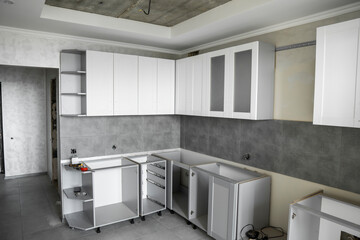 Custom kitchen cabinets installation with a white furniture facades mdf. Gray modular kitchen from chipboard material on a various stages of installation. A frame furniture fronts mdf profile.