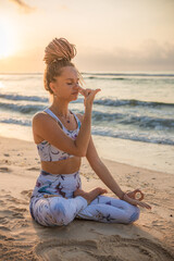 Fototapeta na wymiar Yogi woman sitting in lotus pose, practicing Anuloma Viloma Pranayama, Alternate Nostril Breathing. Control prana, control of breath. Breathing exercise. Sunset. Yoga retreat. Bali