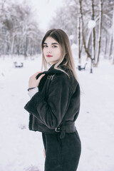 A beautiful young girl in warm clothes walks, plays and poses against the background of a winter snow-covered park and a playground