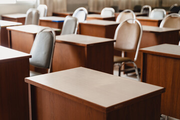 Many wooden tables and chairs well arranged in the university classroom but no student. Empty classroom with no student due to school being lockdown during COVID-19 pandemic.