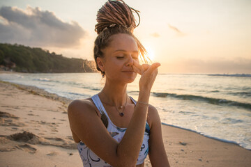 Yogi woman practicing Nadi Shodhana Pranayama, Alternate Nostril Breathing. Control prana, control of breath. Breathing exercise. Sunset time. Yoga retreat. Thomas beach, Bali