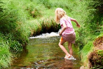 Child cute blond girl playing in the creek. Gril walking in forest stream and exploring nature....