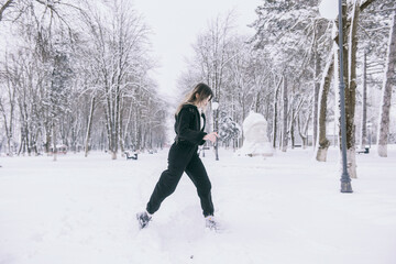 A beautiful young girl in warm clothes walks, plays and poses against the background of a winter snow-covered park and a playground