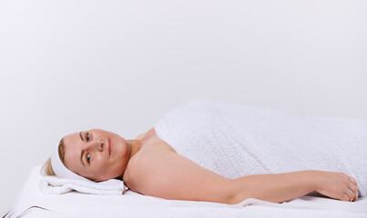 Obraz na płótnie Canvas Caucasian senior woman in a white towel lies in the salon ready for spa treatments on a white background.