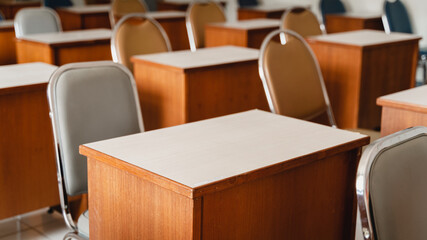 Many wooden tables and chairs well arranged in the university classroom but no student. Empty classroom with no student due to school being lockdown during COVID-19 pandemic.