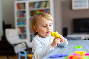 Happy smiling little boy playing with colorful clay alone. Child using plasticine and playing dough.