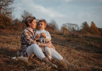 Cheerful pregnant mother spending time with her toddler son in autumnal  park. Mother and son. Family having fun outdoors 